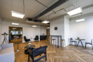Moderne wachtruimte of lounge in een kantoor aan de De Ruijterkade met zithoeken, houten visgraatvloer en strakke verlichting.